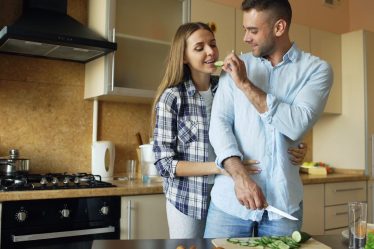 Happy young couple embracing and talking in the kitchen while cooking breakfast at home in the morning