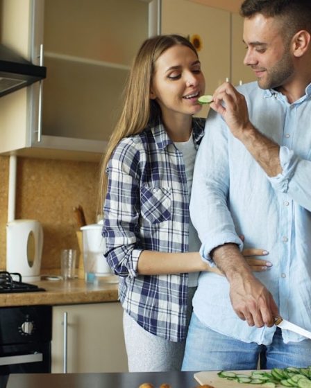 Happy young couple embracing and talking in the kitchen while cooking breakfast at home in the morning