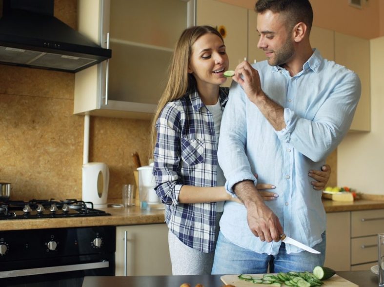 Happy young couple embracing and talking in the kitchen while cooking breakfast at home in the morning